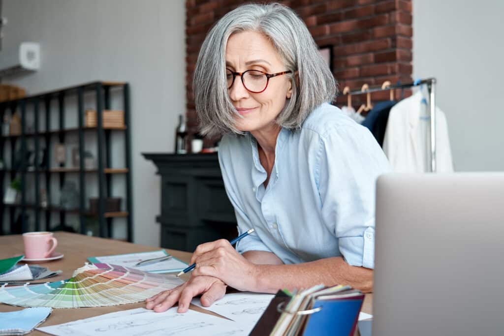 Middle aged stylish woman fashion designer drawing sketches in studio office.