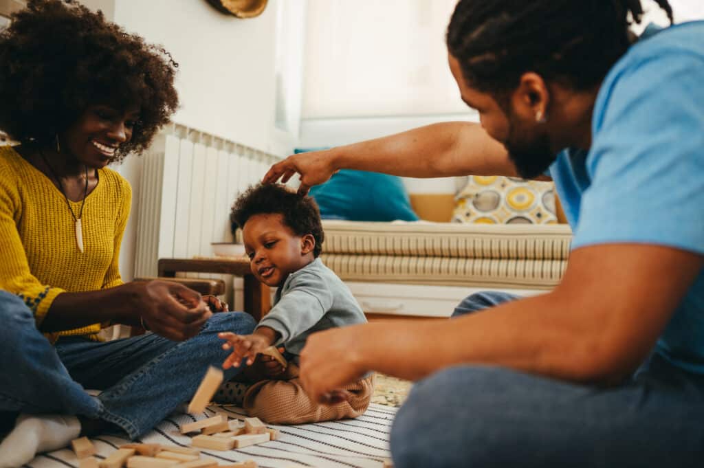 An african american family is having playtime together at home while having fun with a wooden toy.