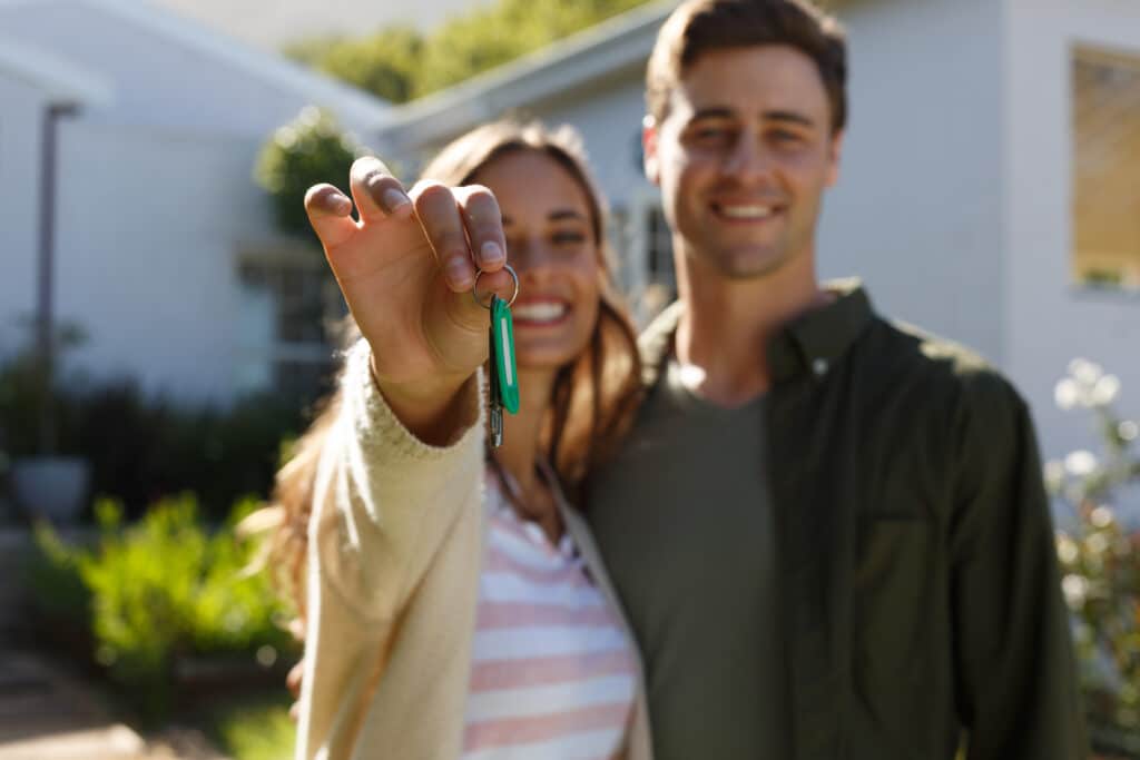 Smiling caucasian couple in garden showing keys to camera. self isolation in new home during covid 19 coronavirus pandemic.