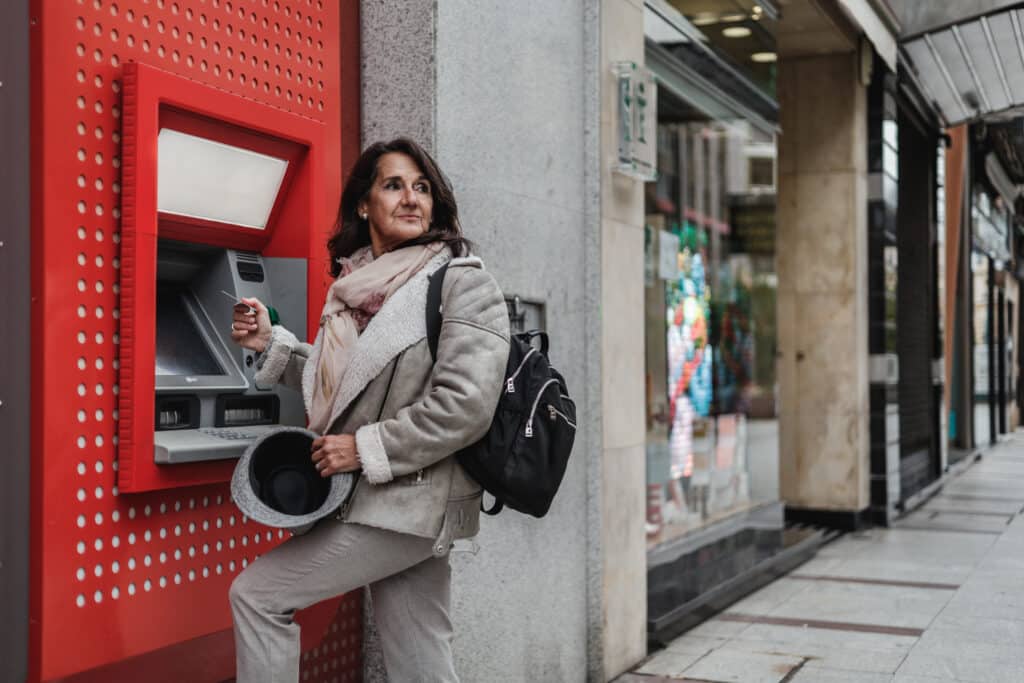 Mature latin woman with credit card in hand withdrawing money from automated teller machine