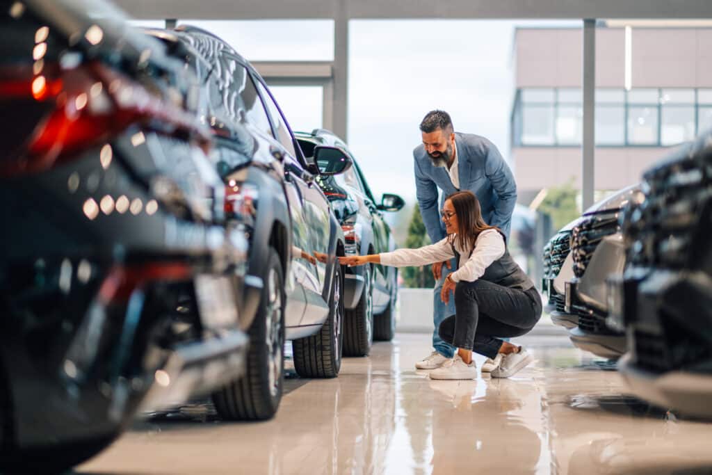 Woman and man examining cars on the showroom floor, discussing details