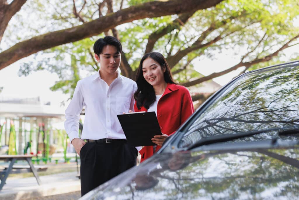 Young asian couple signing car purchase agreement outdoors